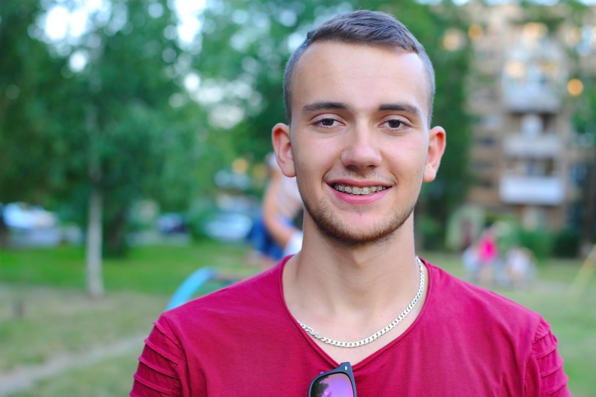 Young man in a red shirt smiles in a park after treatment with Dr. Matthew Noyce at Noyce Orthodontics, your orthodontist in Maryville, MO