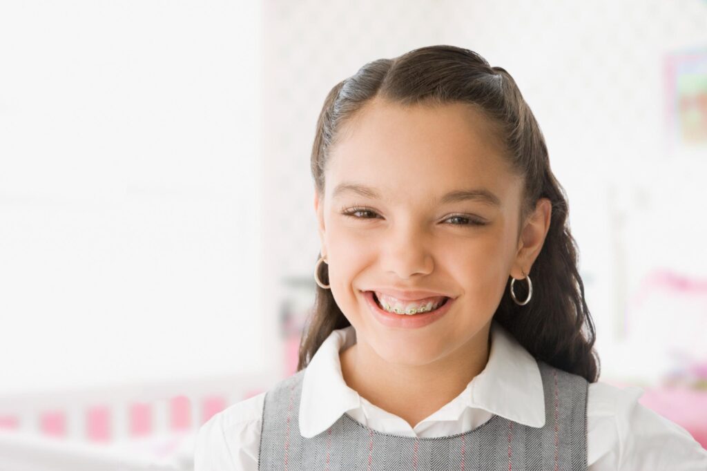 Smiling preteen girl with dark hair pulled back and a white collared shirt, an example of the healthy, straight smiles Dr. Matthew Noyce creates at Noyce Orthodontics in St. Joseph, MO.