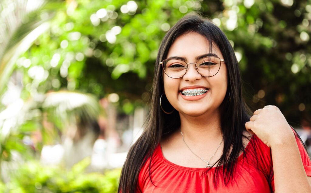 Teenage girl with glasses and braces smiling outdoors, highlighting braces for teens from Dr. Matthew Noyce at Noyce Orthodontics in St. Joseph & Maryville, MO.